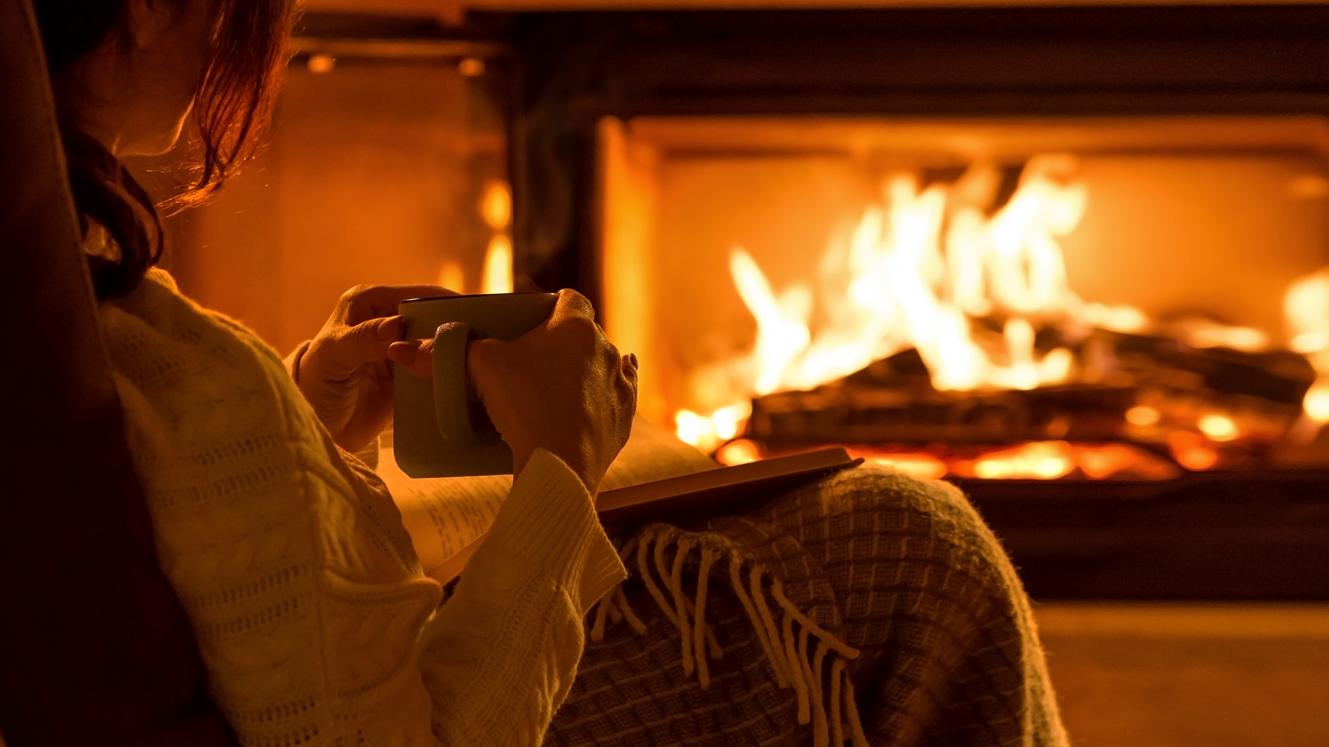 Young Woman Sitting At Home By The Fireplace And Reading